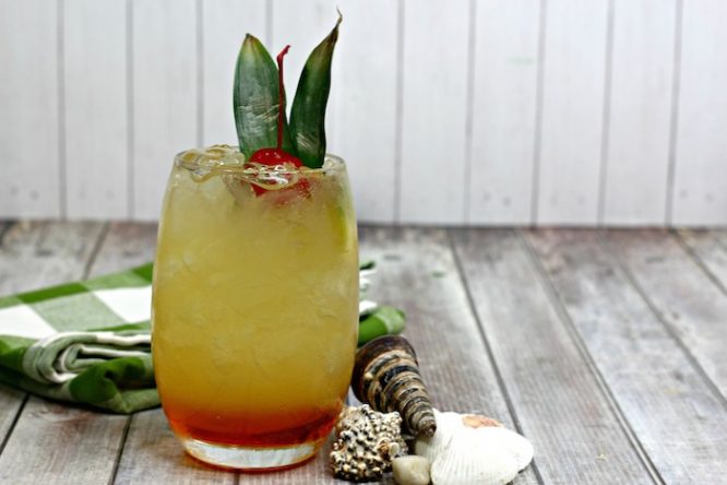 Orange and Pineapple Hawaiian Hammer layered cocktail on a green check napkin and seashell decorations